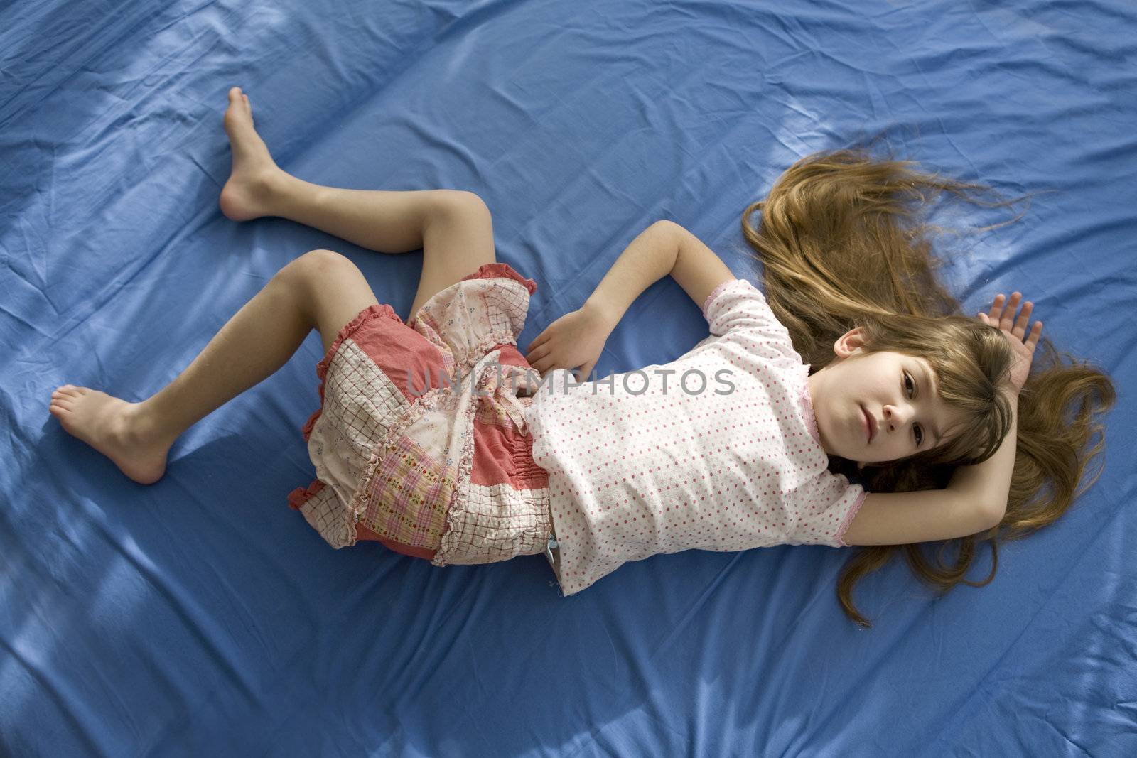 little adorable girl lying on the bed. Blue cotton sheet by elenarostunova