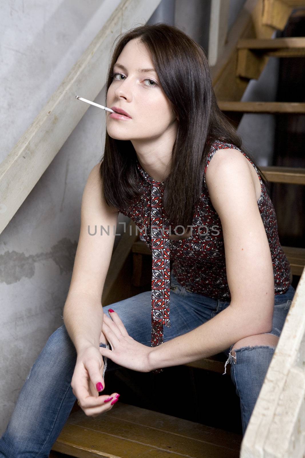 young attractive smoking  girl in jeans having a hole sitting on by elenarostunova