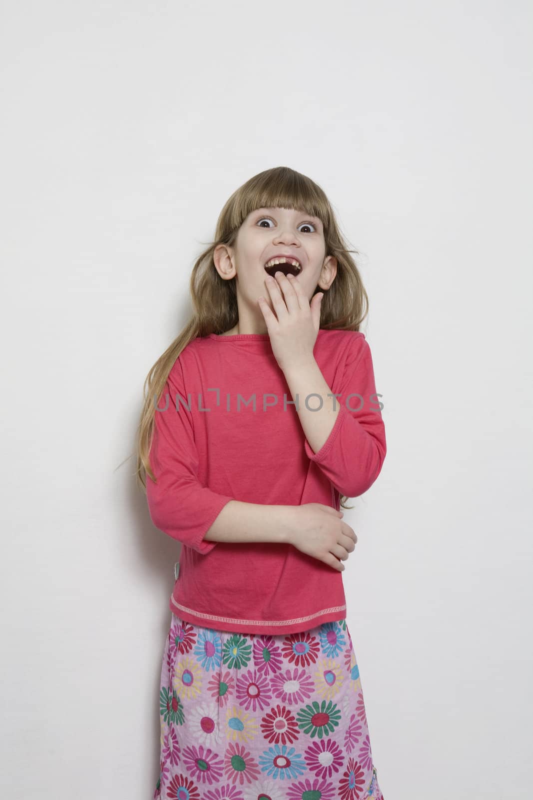 portrait of young smiling cute astonished girl seven years old. Isolated. Her hands close mouth