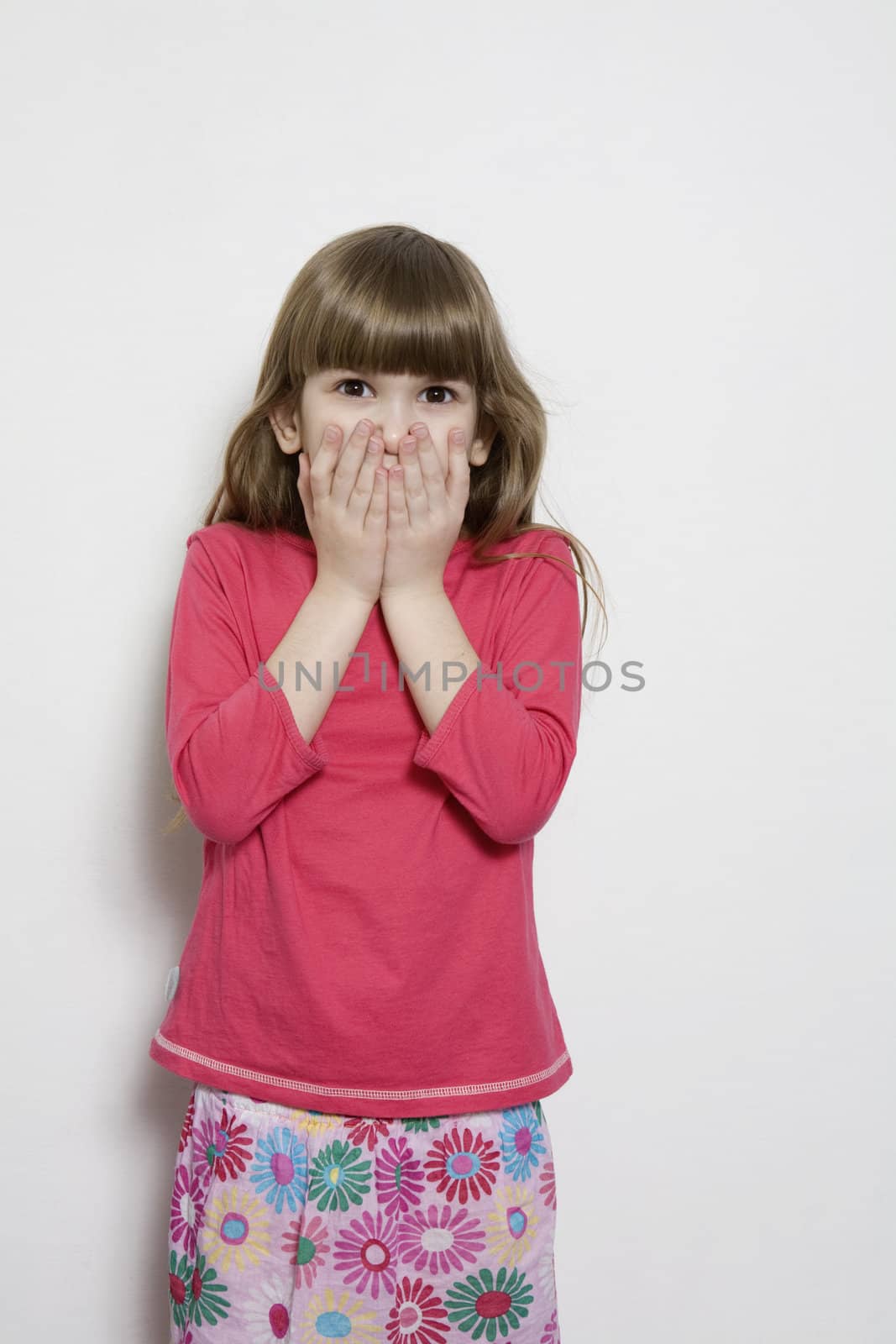 portrait of young smiling cute astonished girl seven years old. Isolated. Her hands close mouth