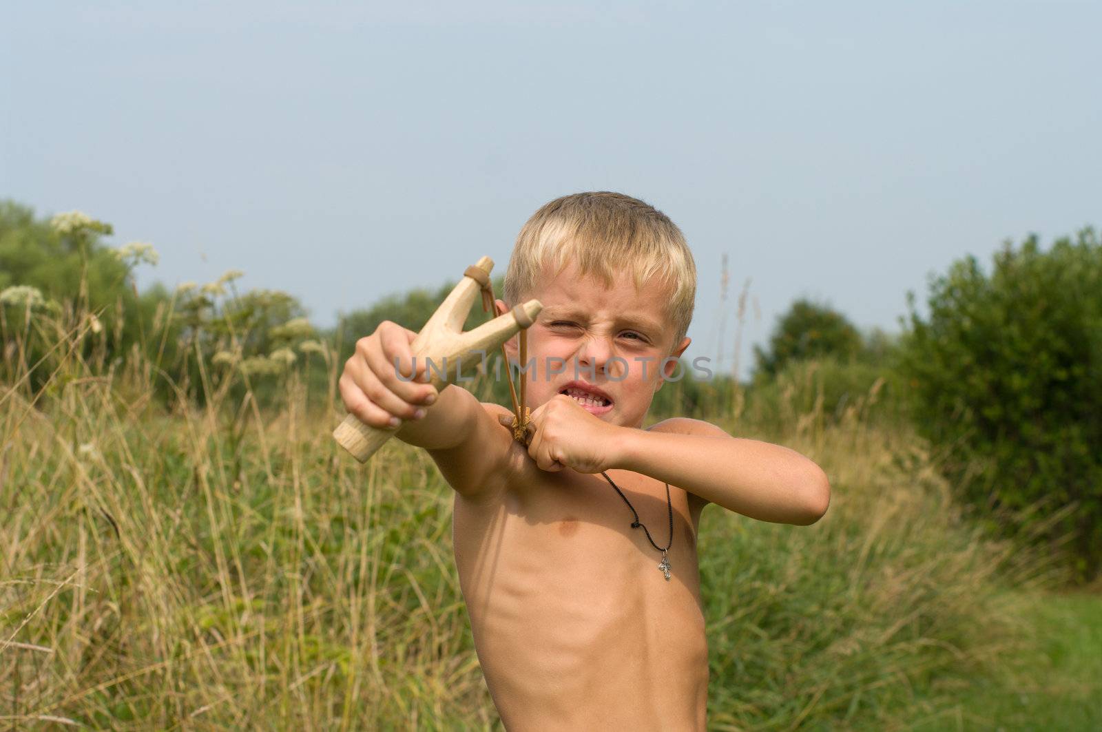 The boy aims from a wooden slingshot in the afternoon.