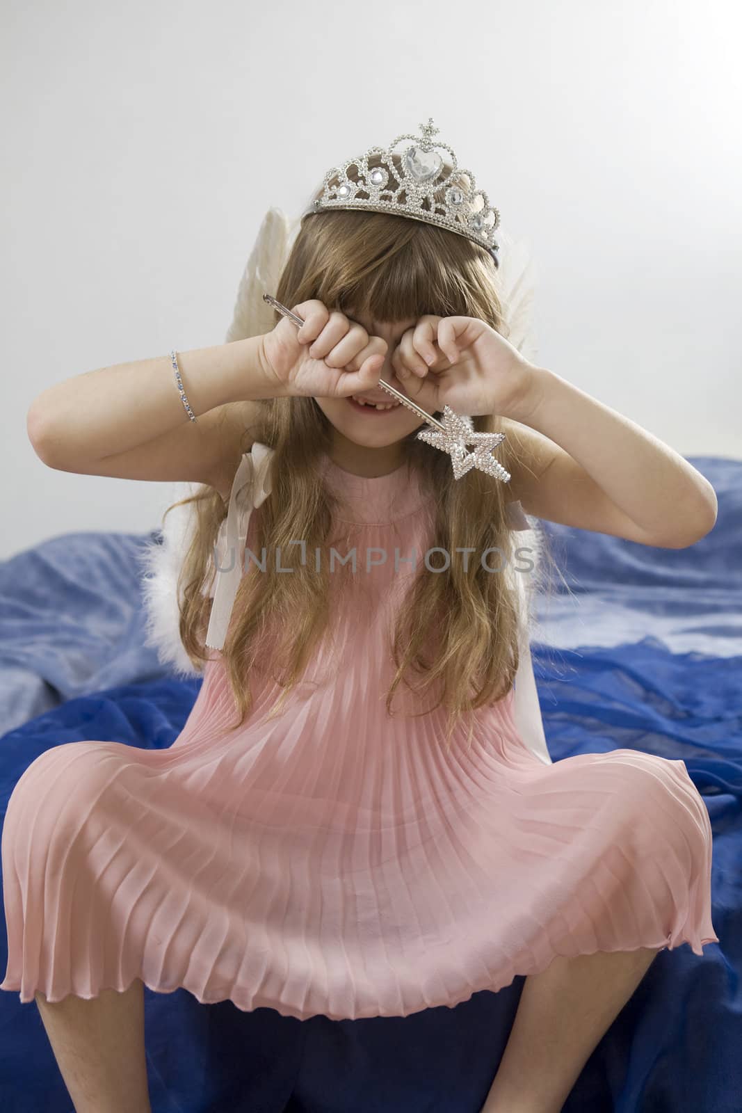 Holiday was bad. Little cute girl seven years old wearing angel`s wing and crown sitting on bed