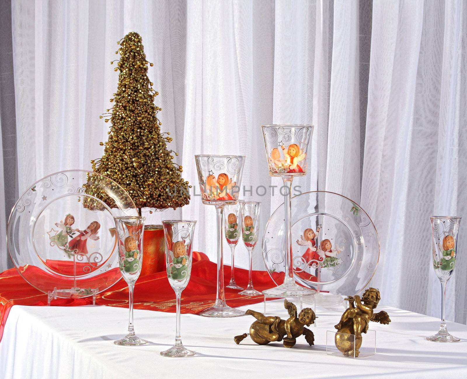 The Christmas still life consisting of glass glasses, plates, candlesticks, bronze angels and decorative fur-tree.