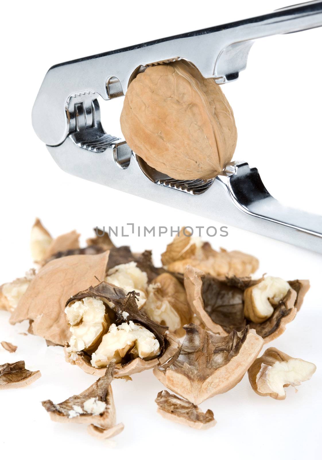 Metal nutcracker with crushed walnuts on white background