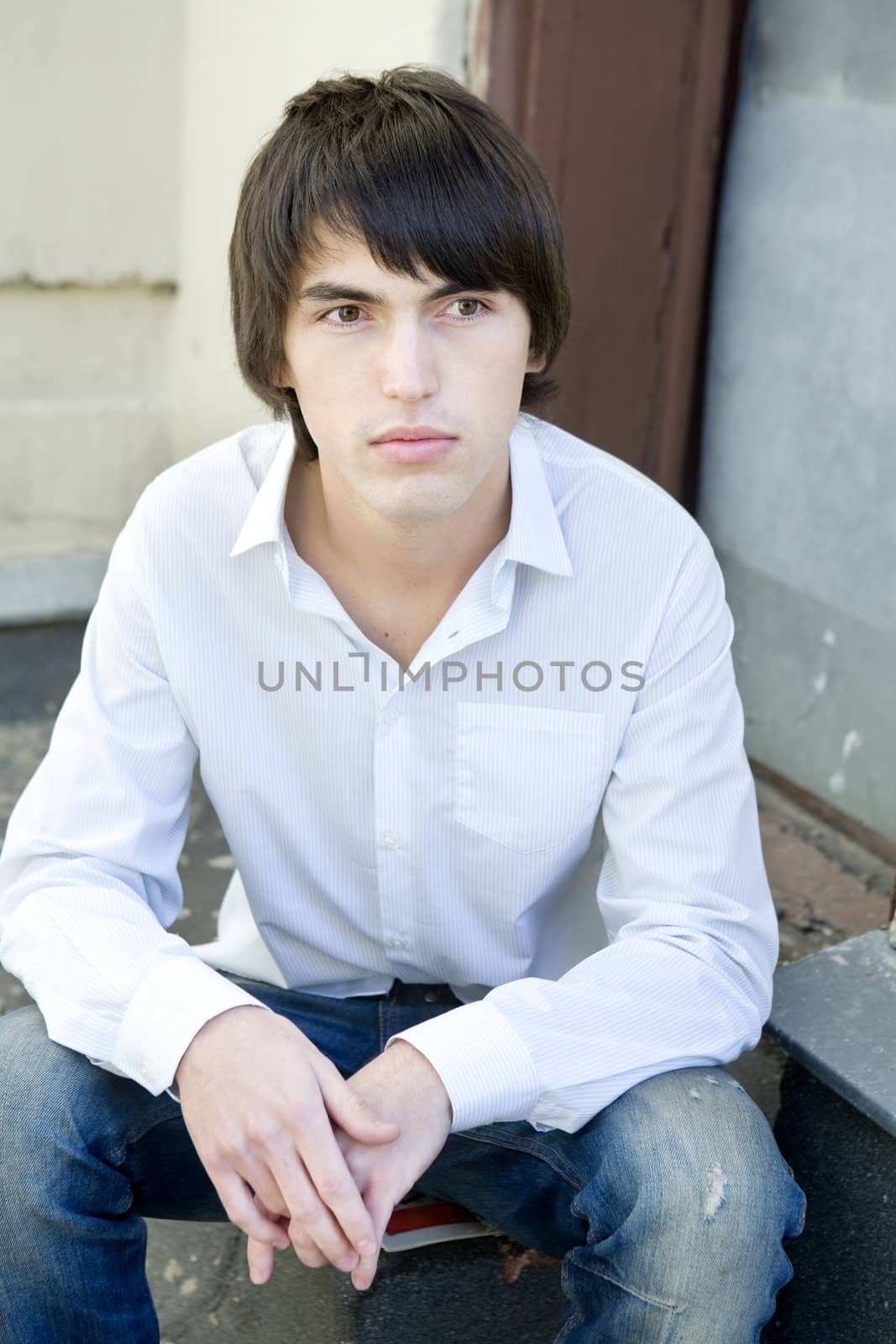 close up portrait of young serious handsome man sitting on on the doorstep.