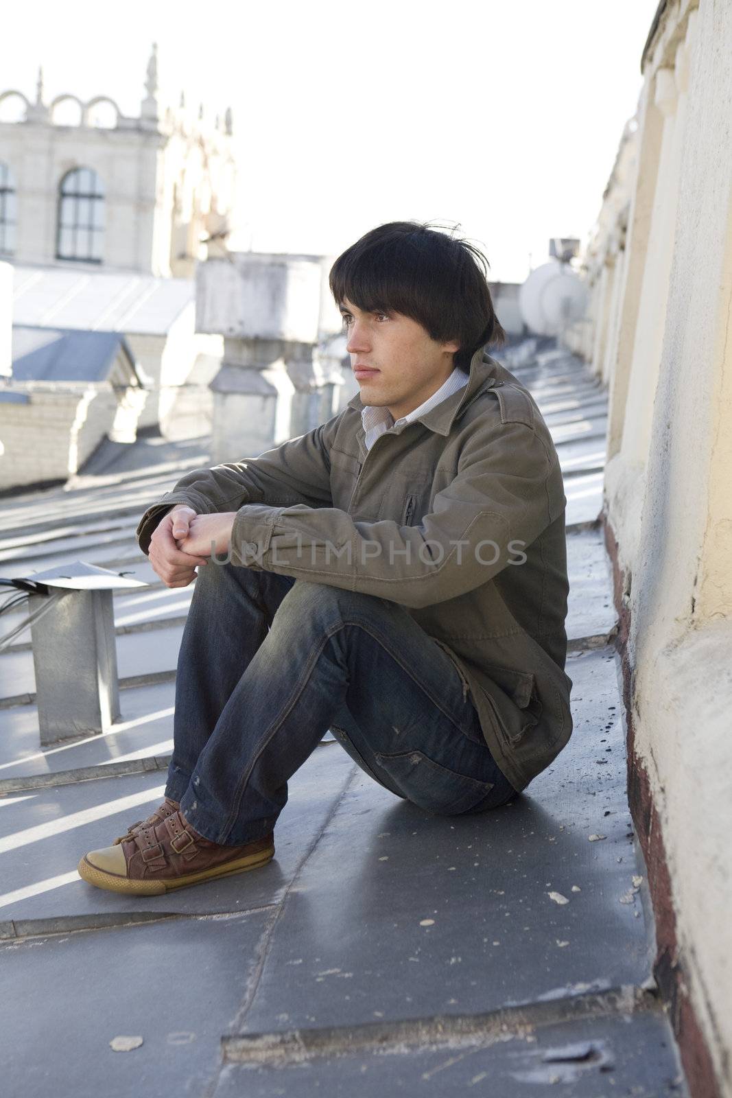 close up portrait of young serious handsome man sitting on on the roof.