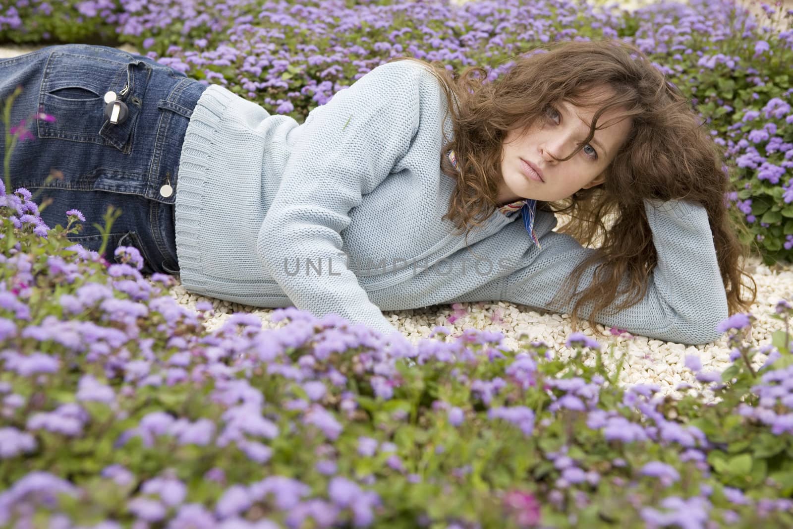 Attractive young serious woman lying between blue flower on white stone