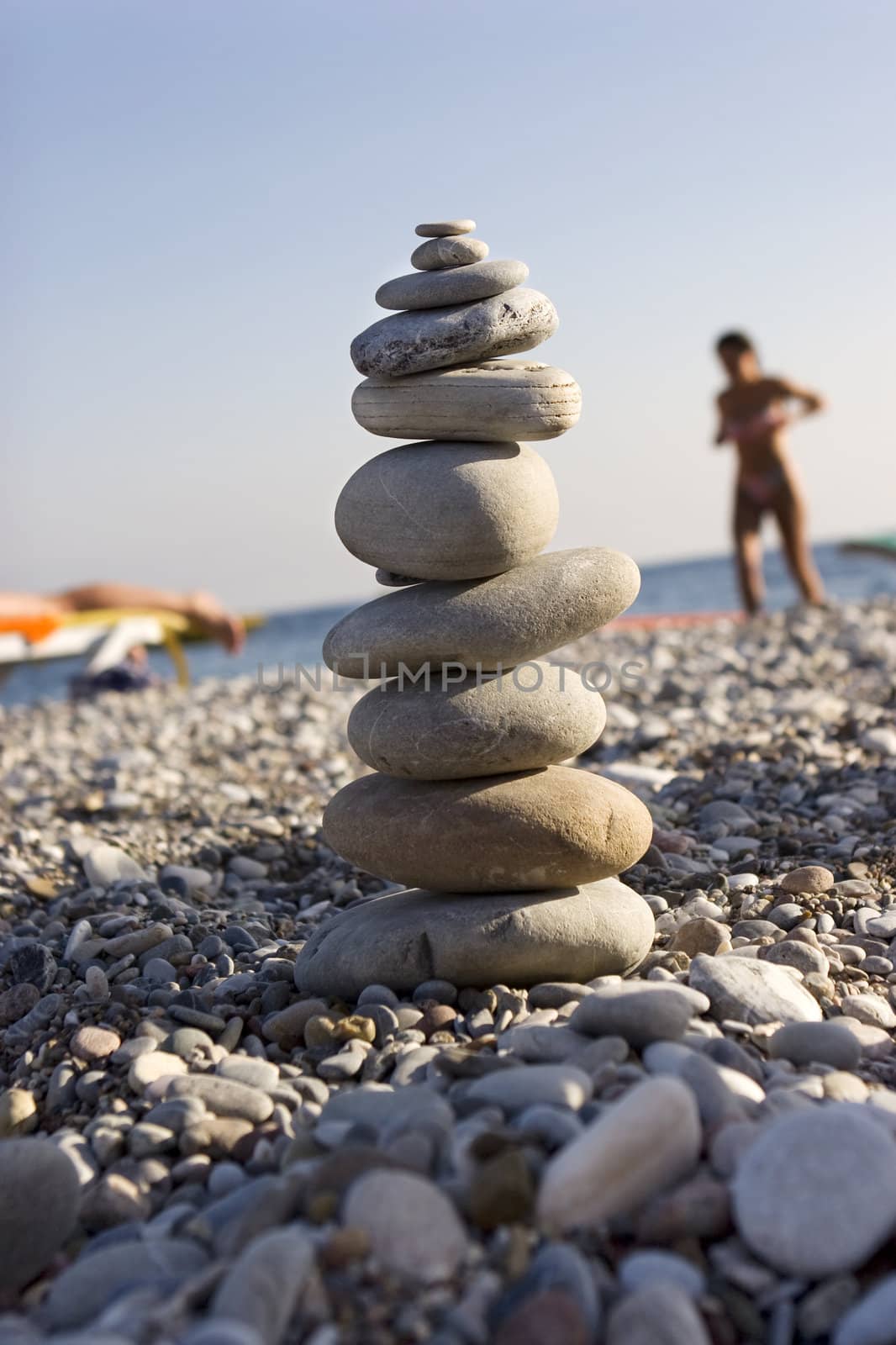 Six differently colored and sized pebbles stacked on a beach by elenarostunova