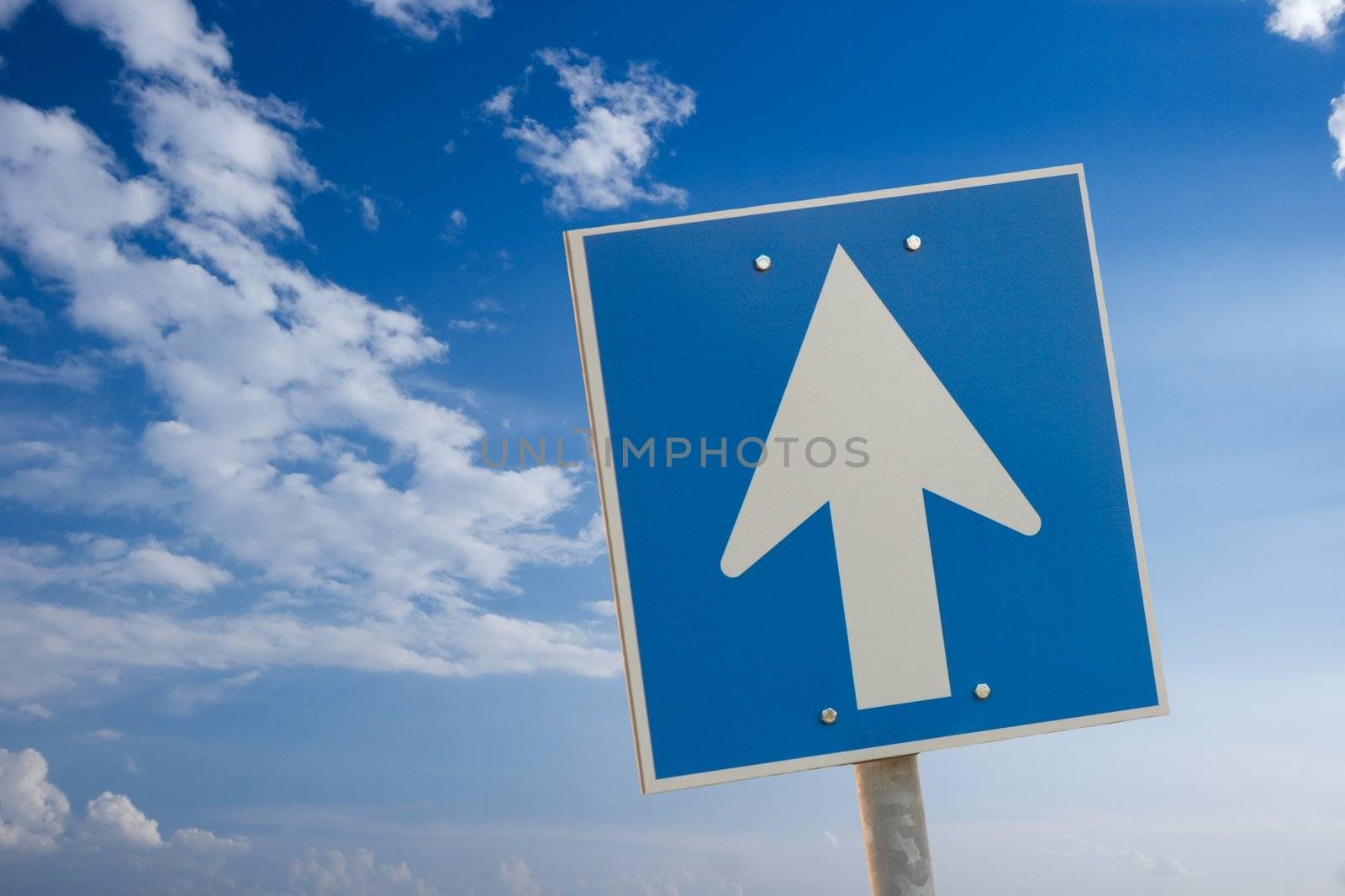 Arrow sign against bright blue sky with white clouds