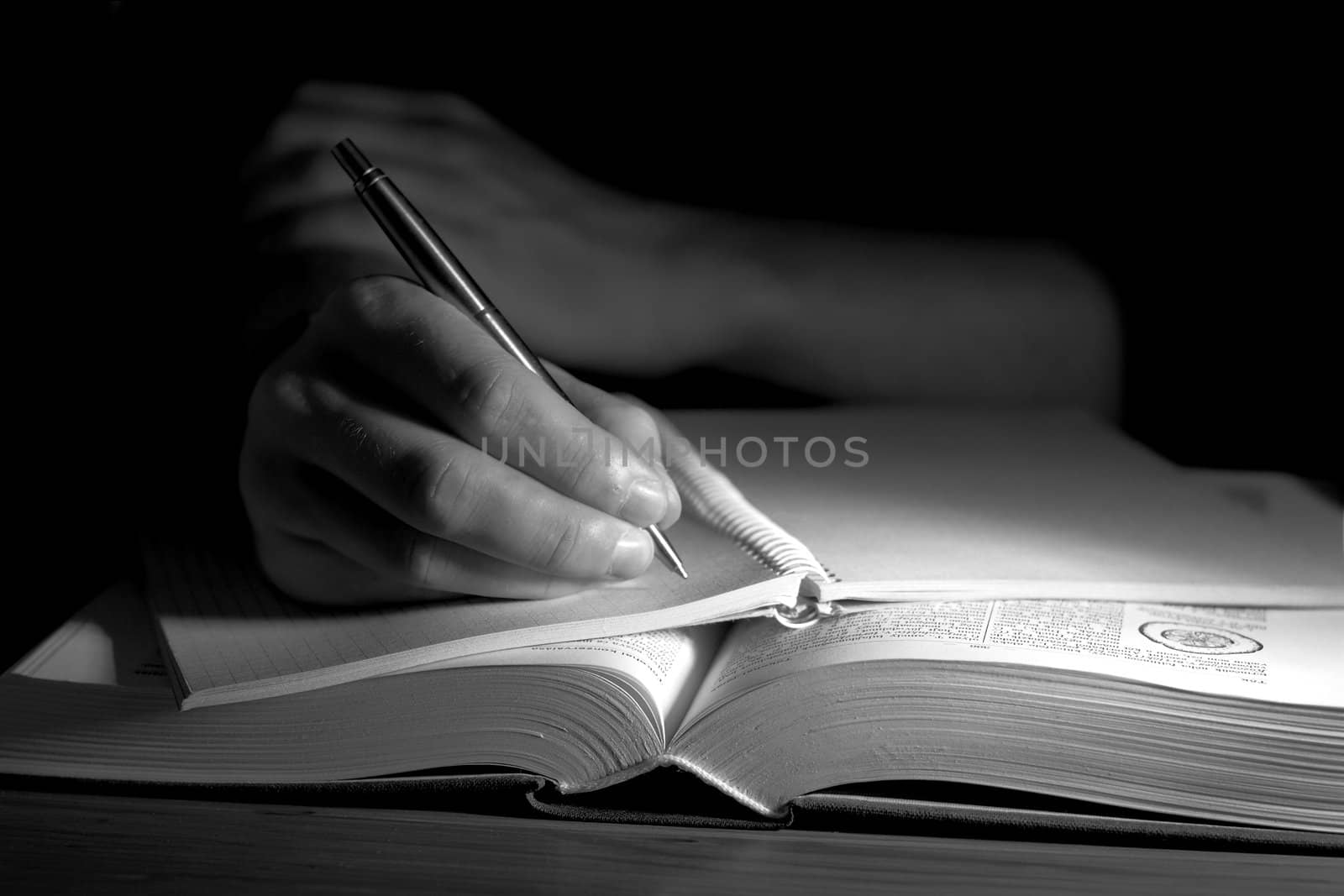 Open book in a dark room, with human hand taking notes