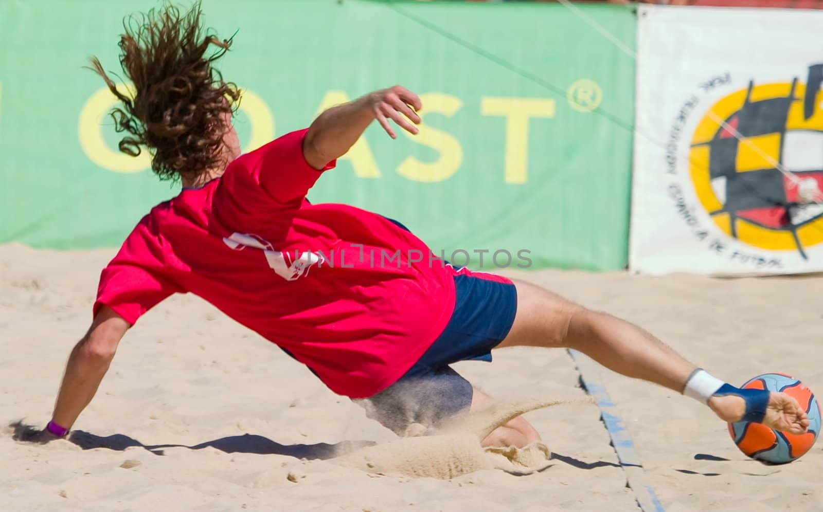 Player gliding over the sand to avoid that the ball comes out of the field