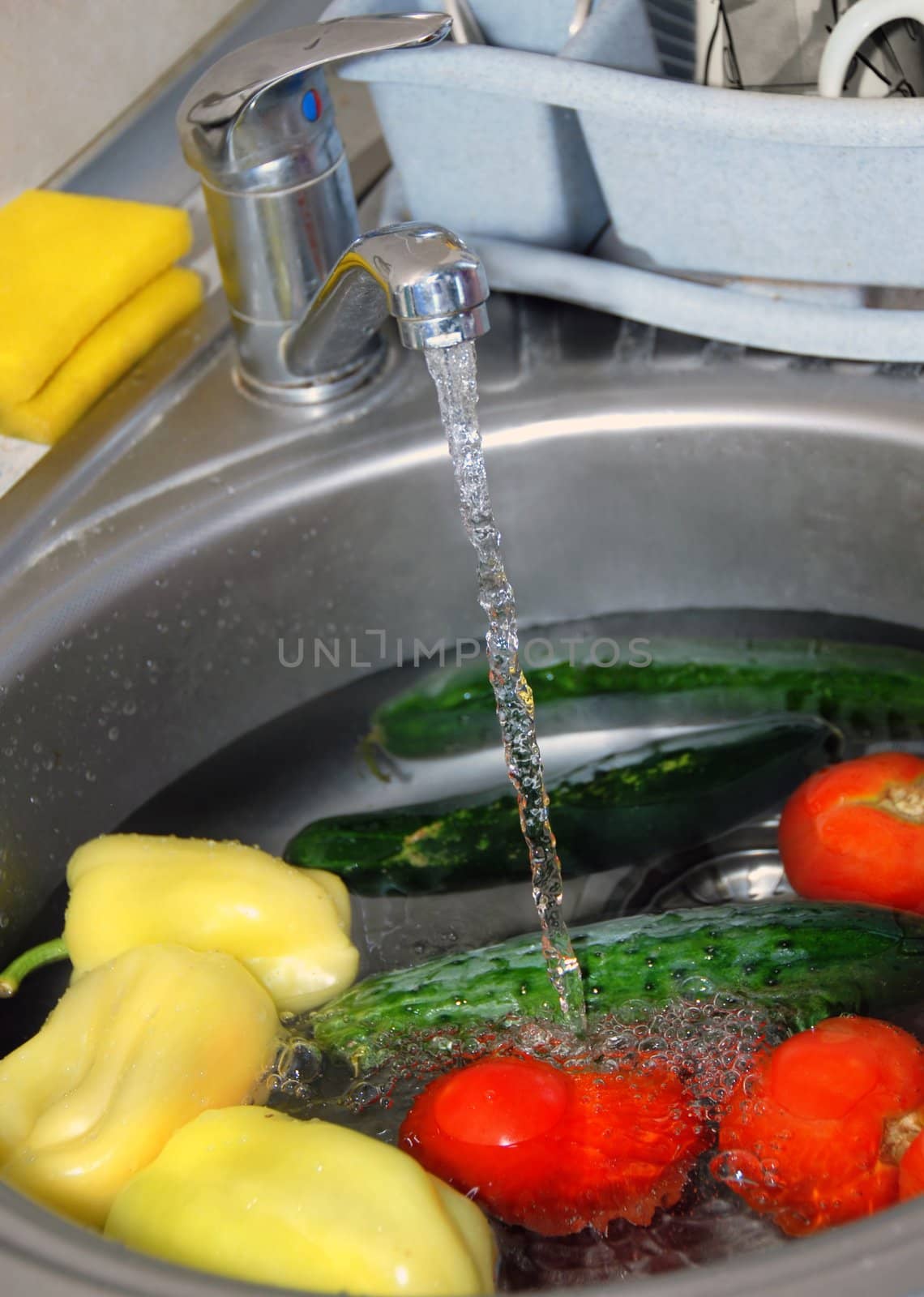 washing tomatoes, cucumbers and paprika in water in kitchen sink