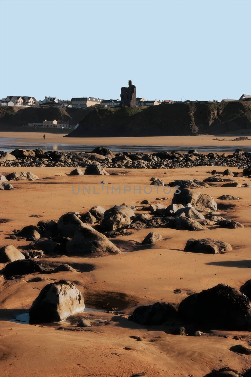 a rocky beach on a warm day with a calm sea and someone walking in the background