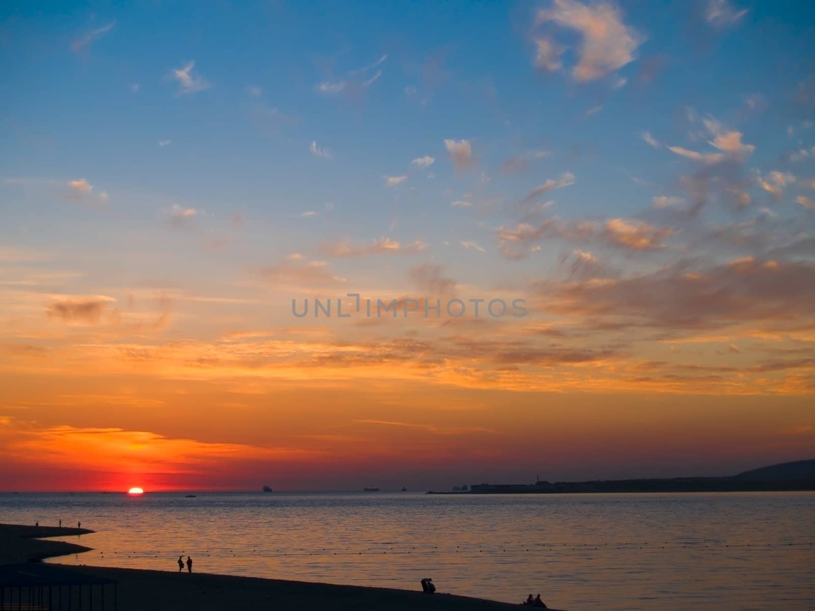 Wonderful sunset in a bay with coastline and walking peoples silhouettes