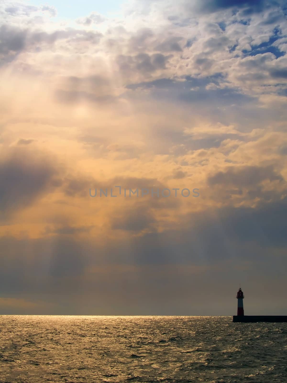 Sunset with visible sunrays in sea with lighthouse