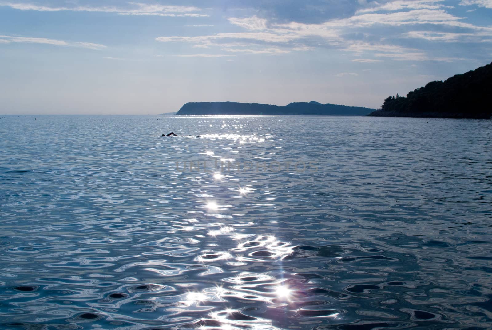 Backlit silhouette of lone swimmer in a bay with the sun shining and reflecting off the waves