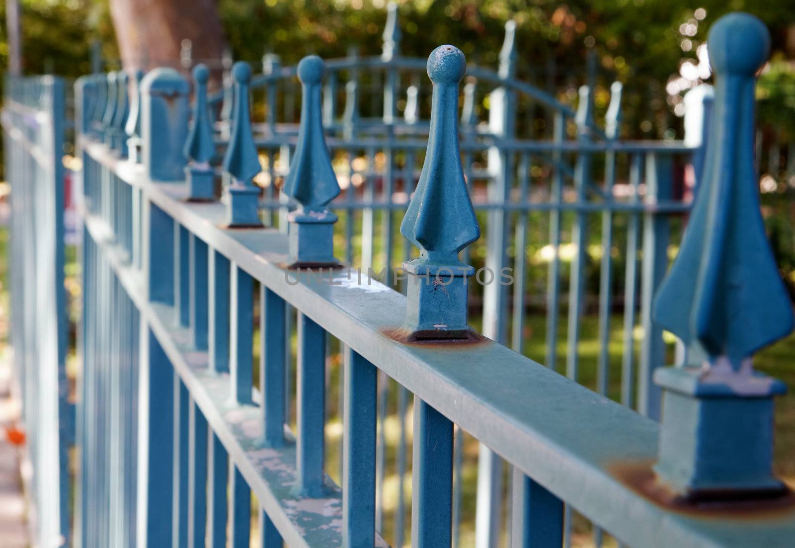 Blue metal spiked residential fence diminishing to soft focus in the distance