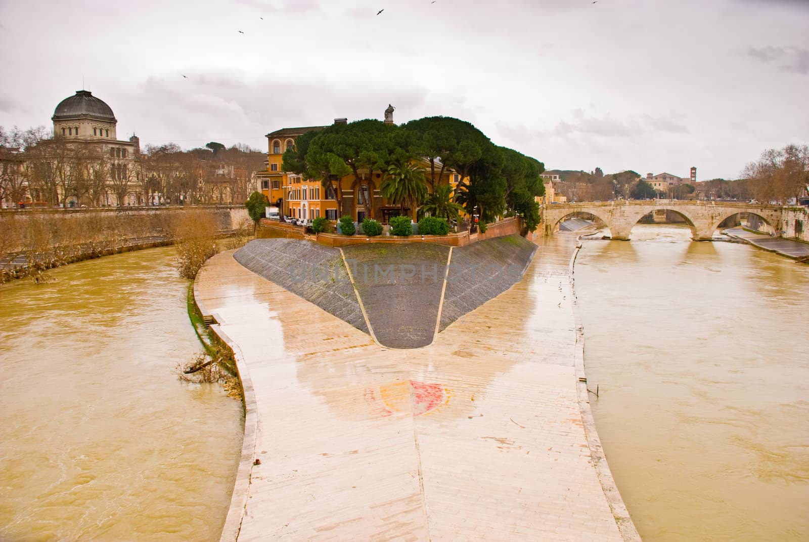 View across the River Tiber to Isola Tiberina in Rome. The island was modeled to resemble a ship by the romans in the 2nd century BC