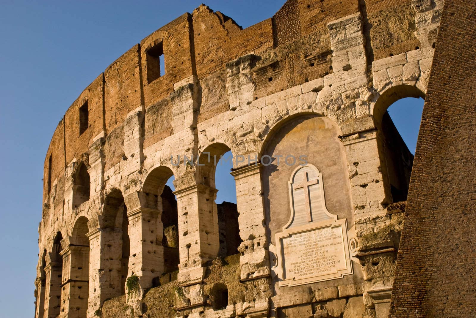 Lateral view of the Colosseum Amphitheater in Rome against blue sky background.