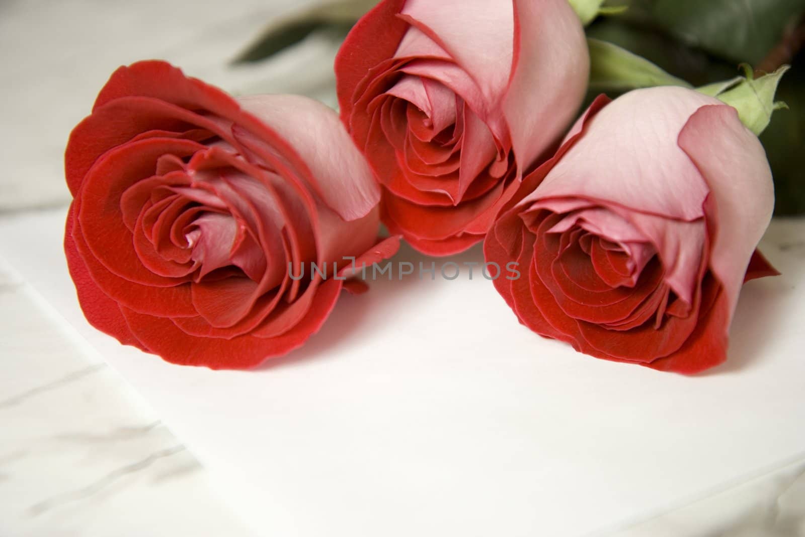 Three red roses and note on a marble table
