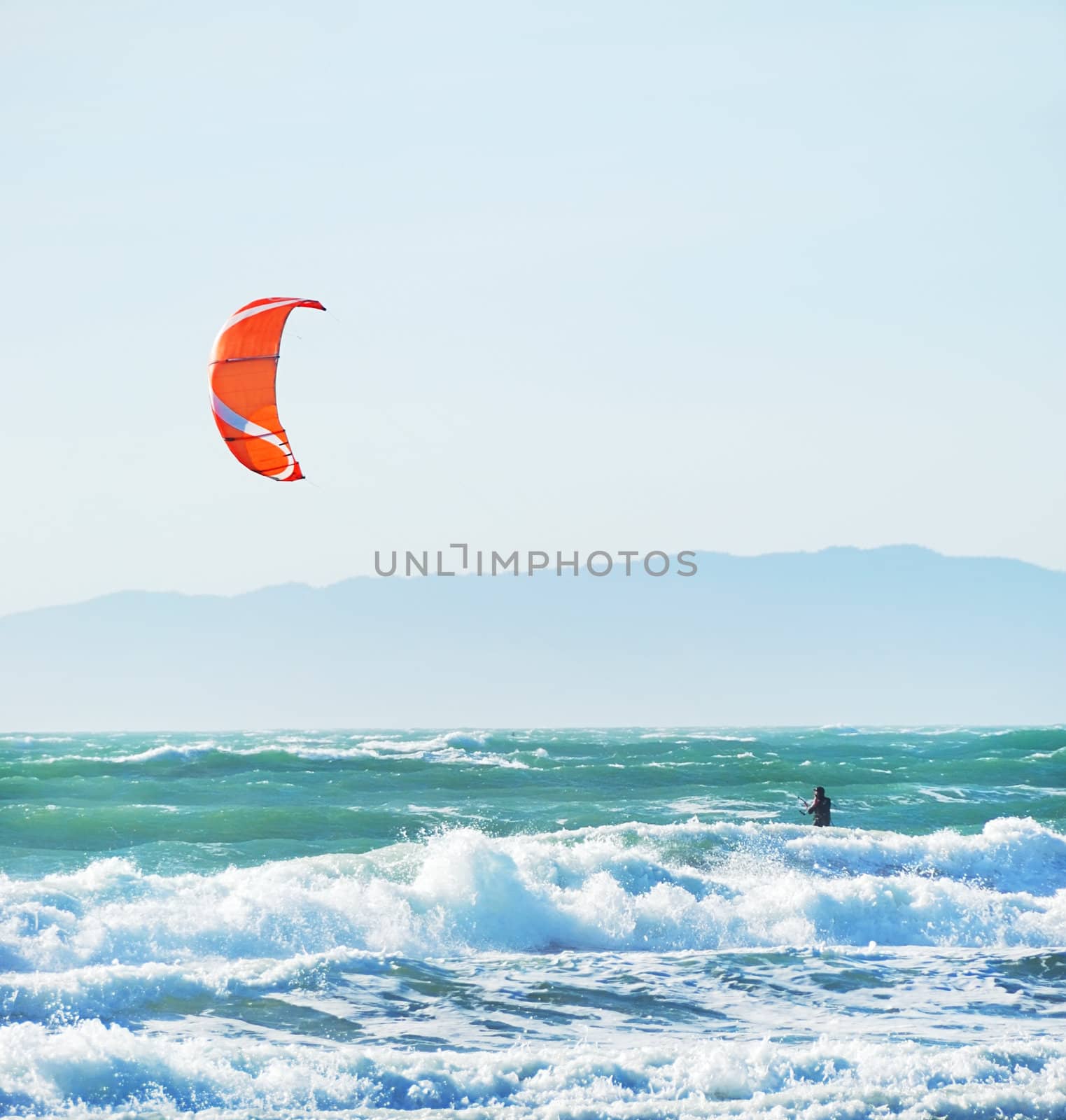 Surfer with red kite surfing off the beach in San Francisco, California on a sunny day.