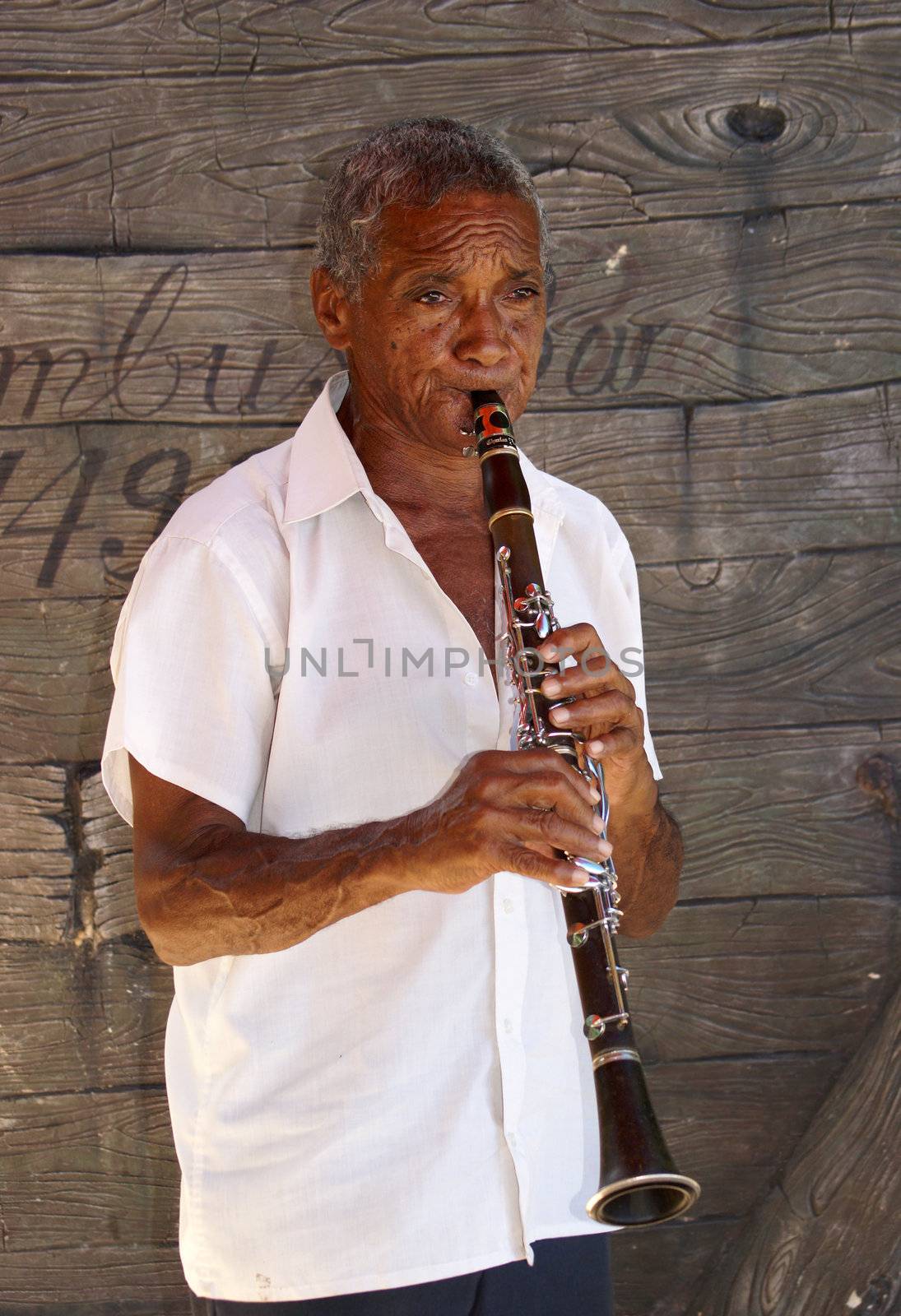 An elderly Cuban man is playing the clarinet in front of a boat at Guardalavaca, Cuba on October 11, 2010.