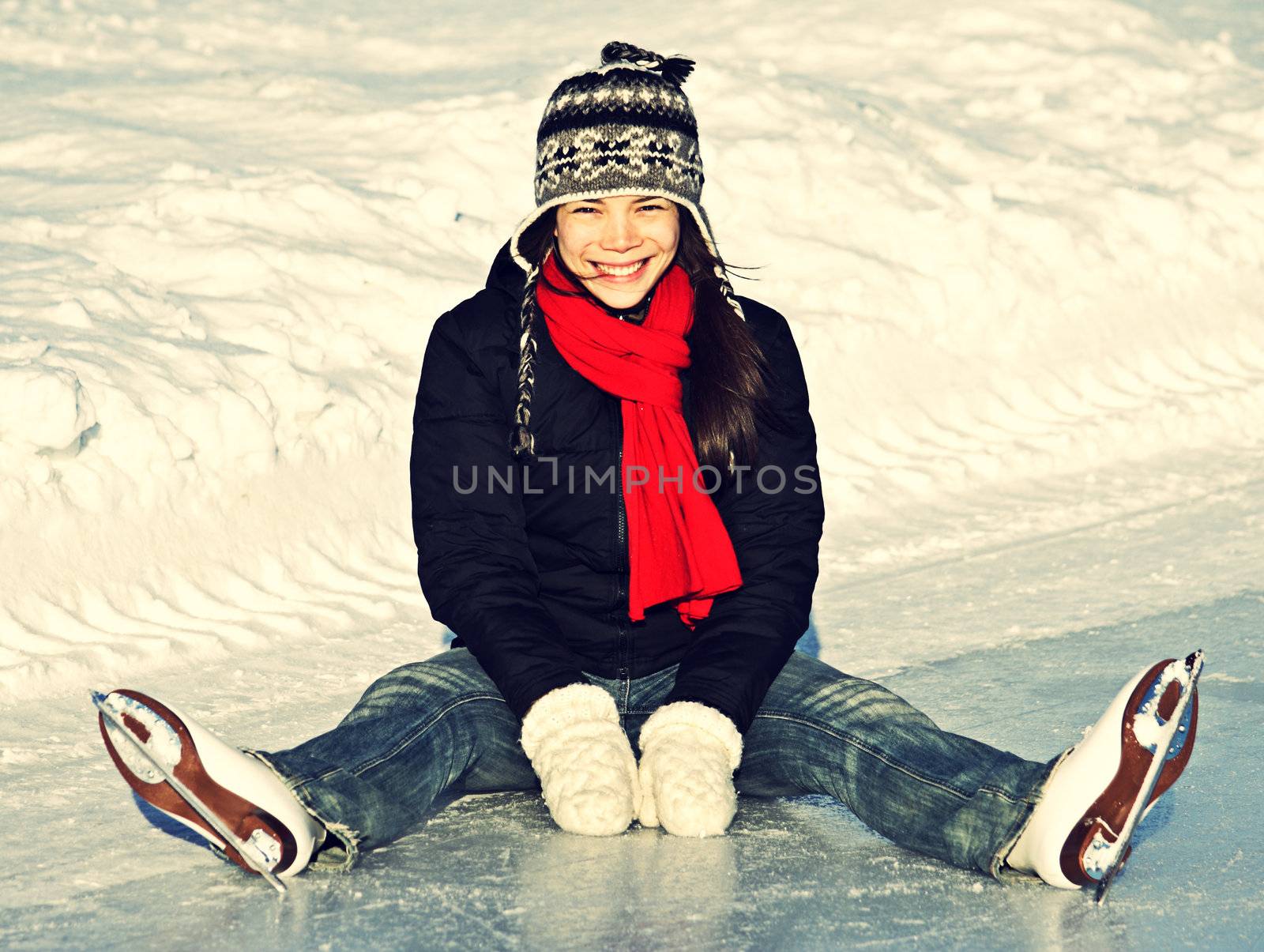 Ice skating woman sitting on the ice smiling.