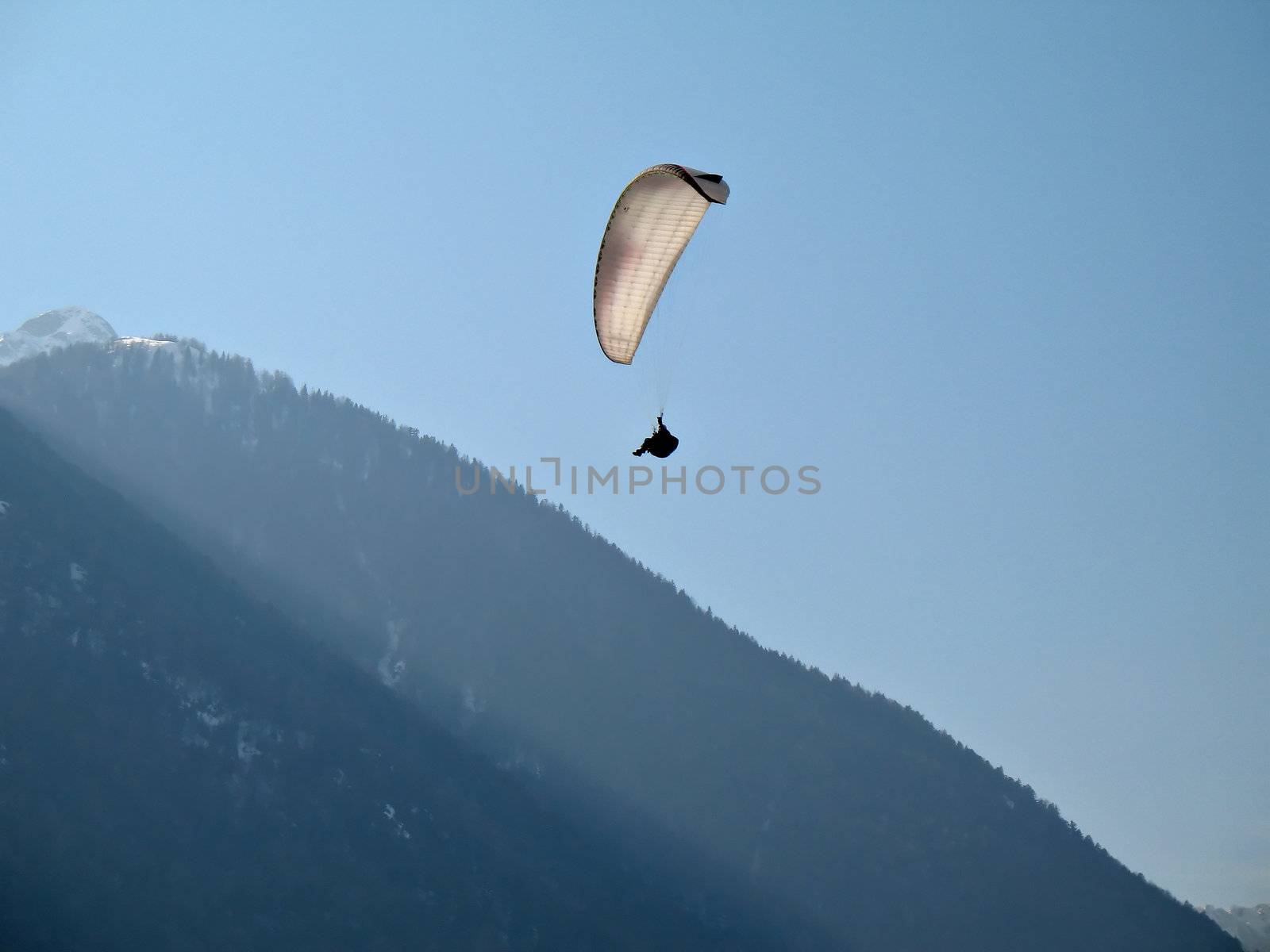 A paraglider il flying in the blue sky near a mountain with his paraglide