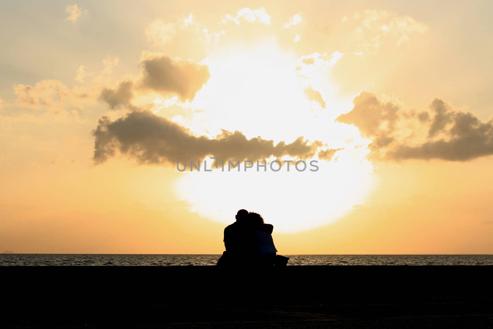 a couple sitting together at the sunset by yucelunal