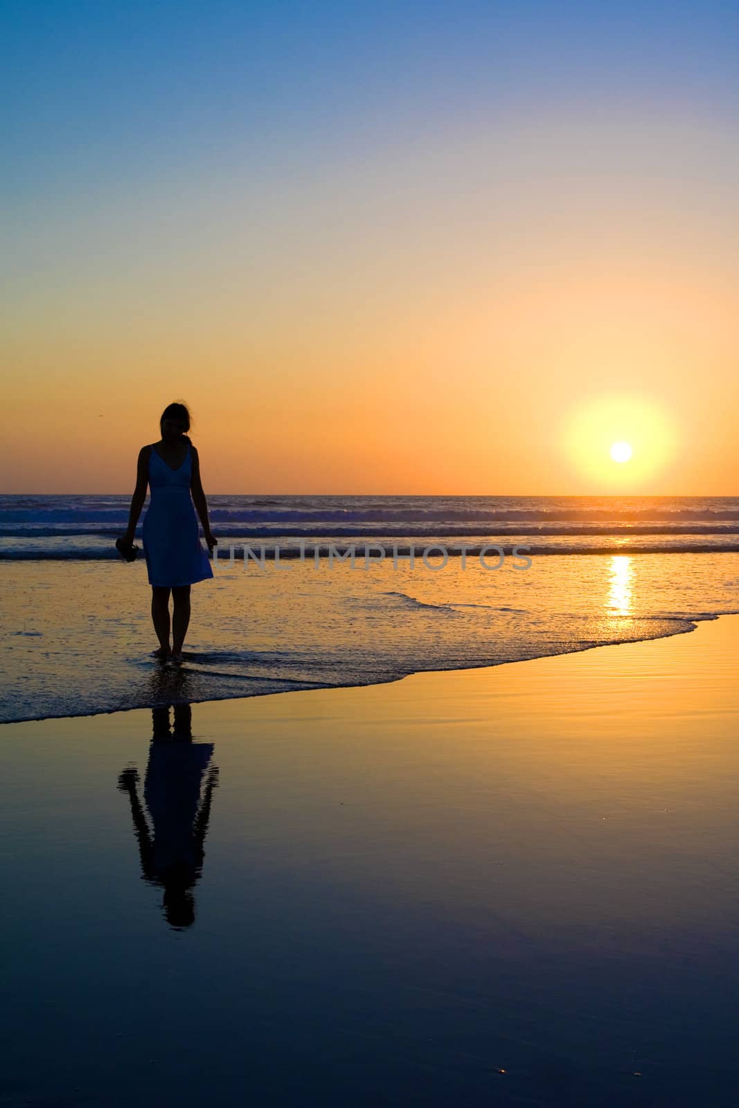 Woman walking on the beach at sunset.