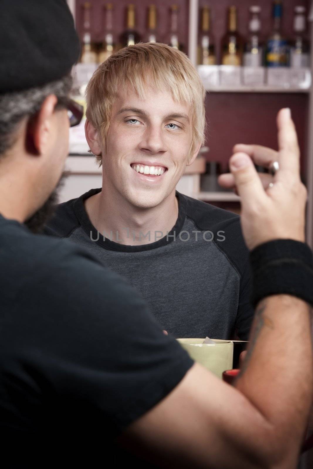 Cheerful young blonde man reacting to coffee house conversation