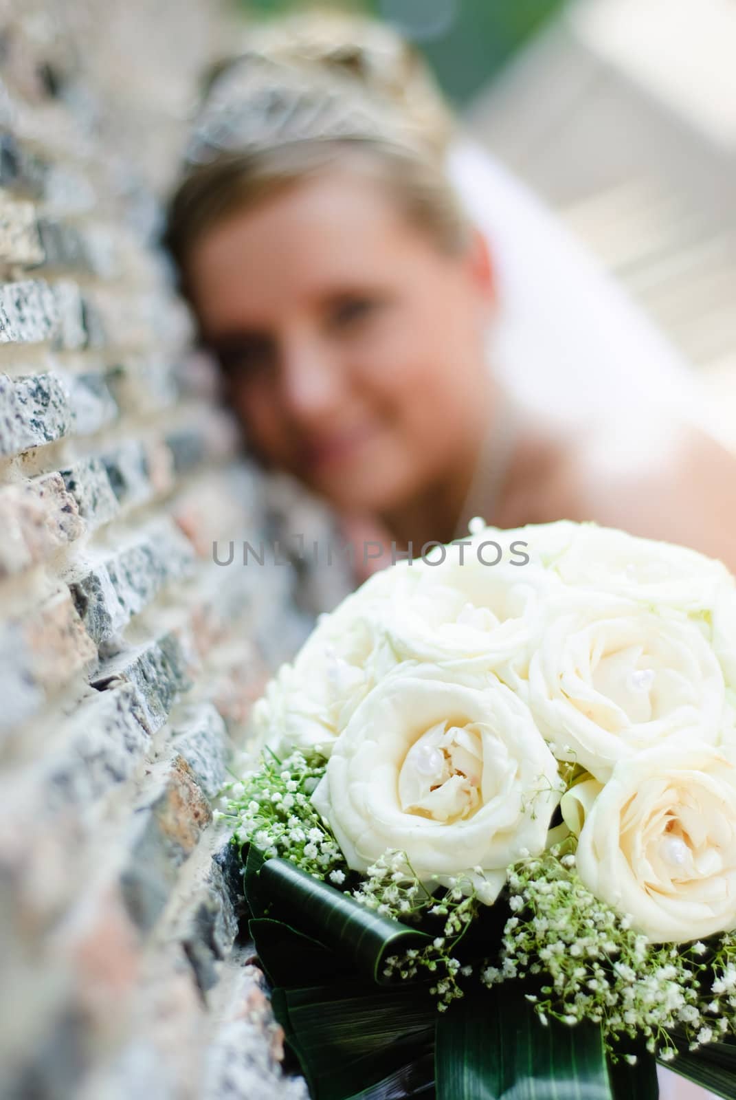 bridal bouquet of white roses and blurred bride near the wall at background