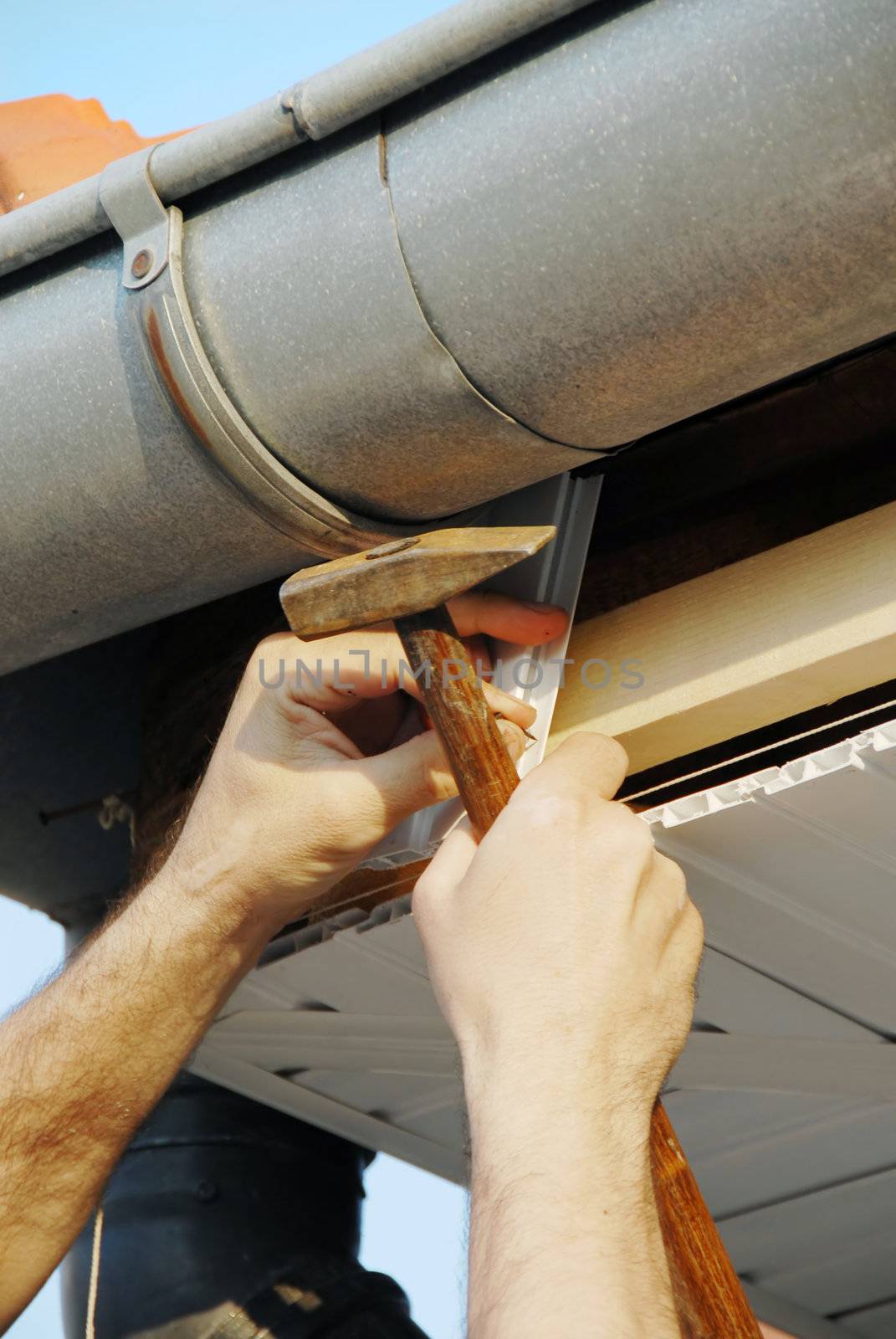 working hand with hammer and nail under house roof outdoor