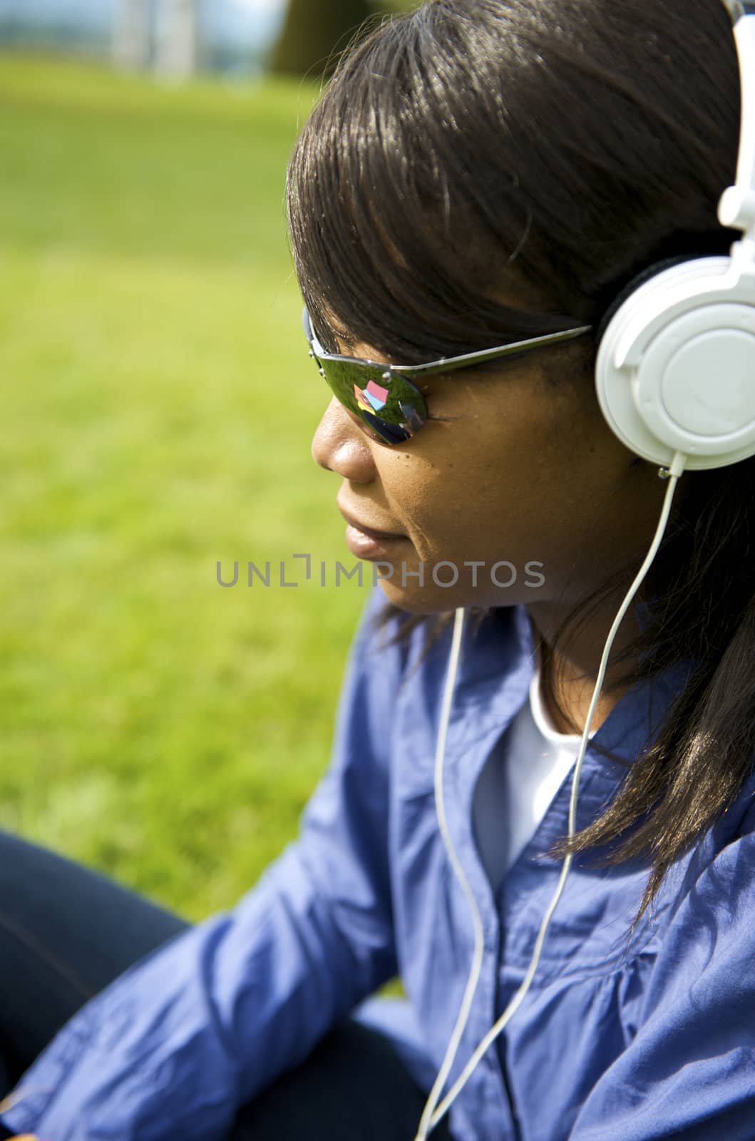 Black woman listening to the music in a park with white headphones