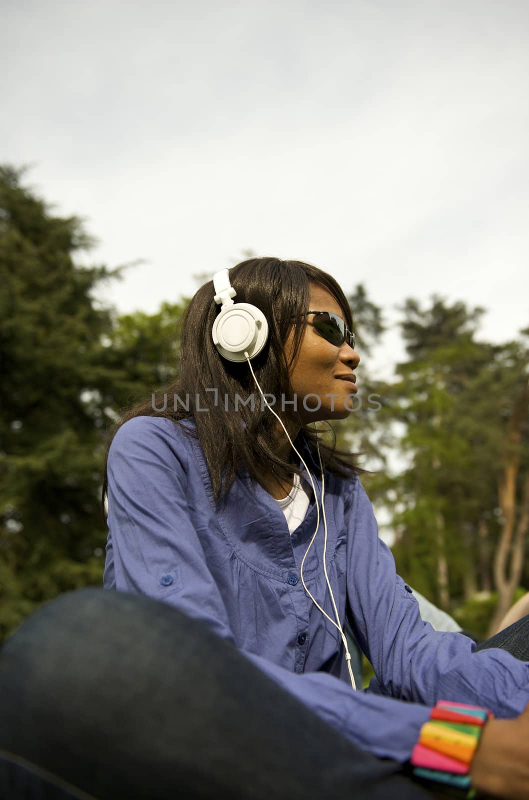 Black woman listening to the music in a park with white headphones