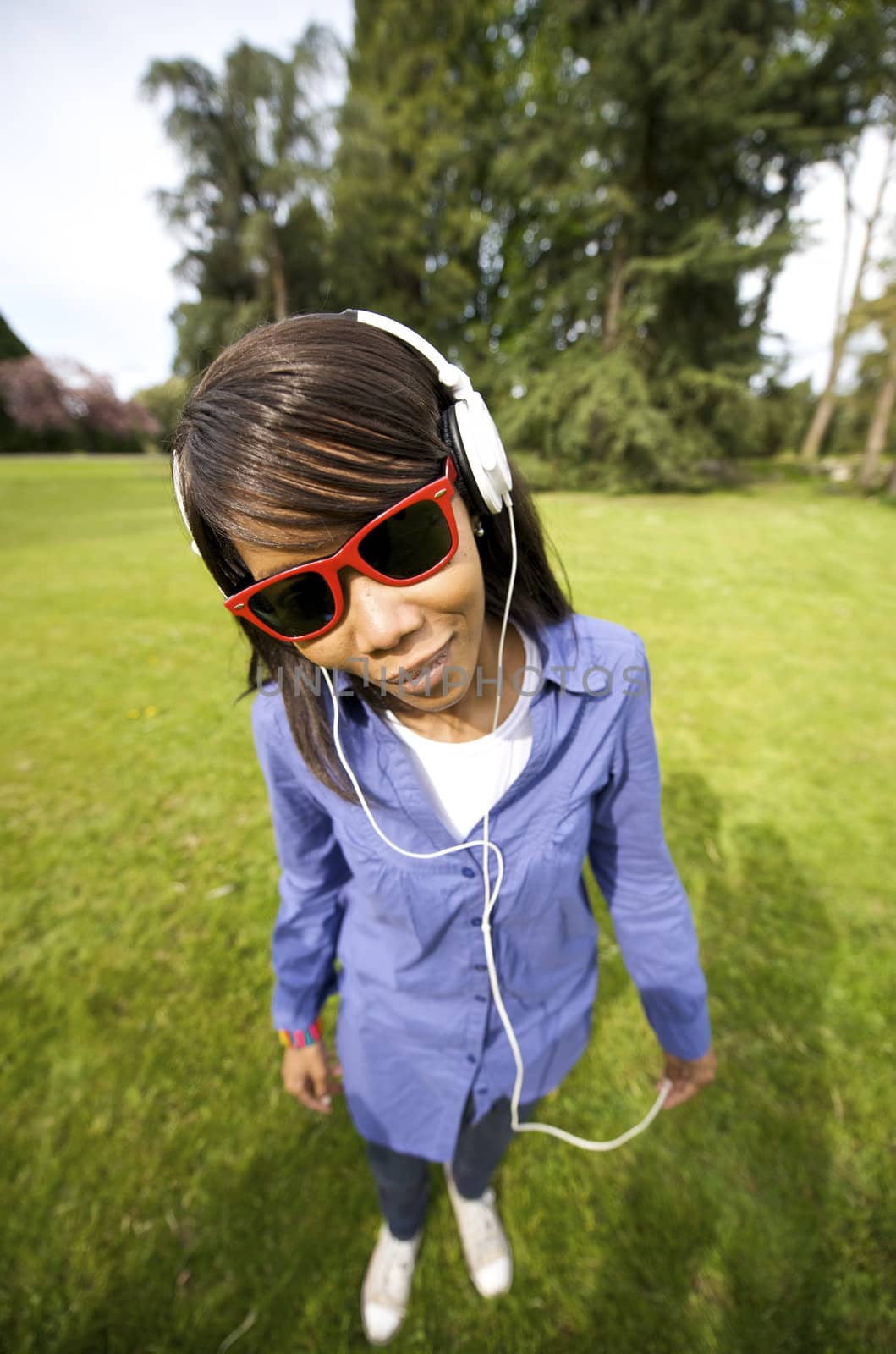 Black woman listening to the music in a park with white headphones