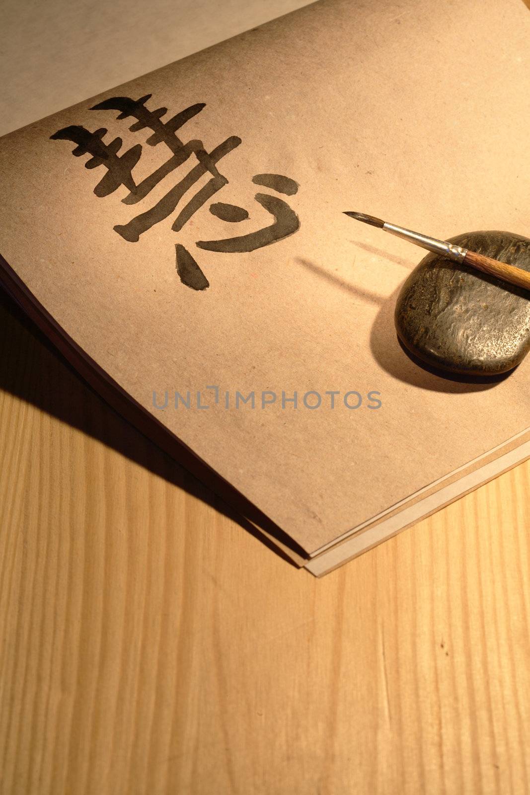 Paintbrush lying on black stone near paper with chinese symbol WISDOM on wooden background
