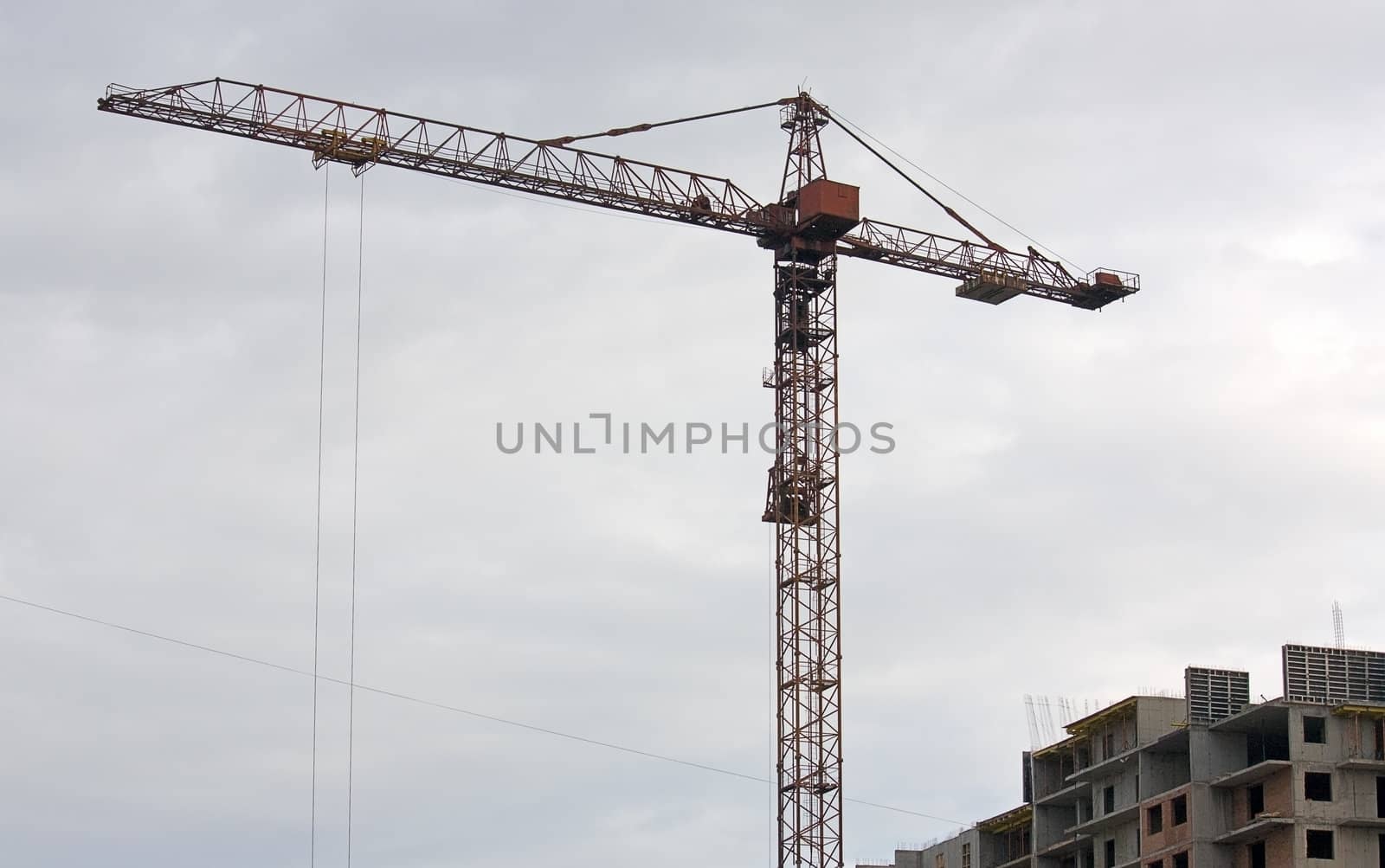 Tower crane near the house under construction on the background of a cloudy sky.