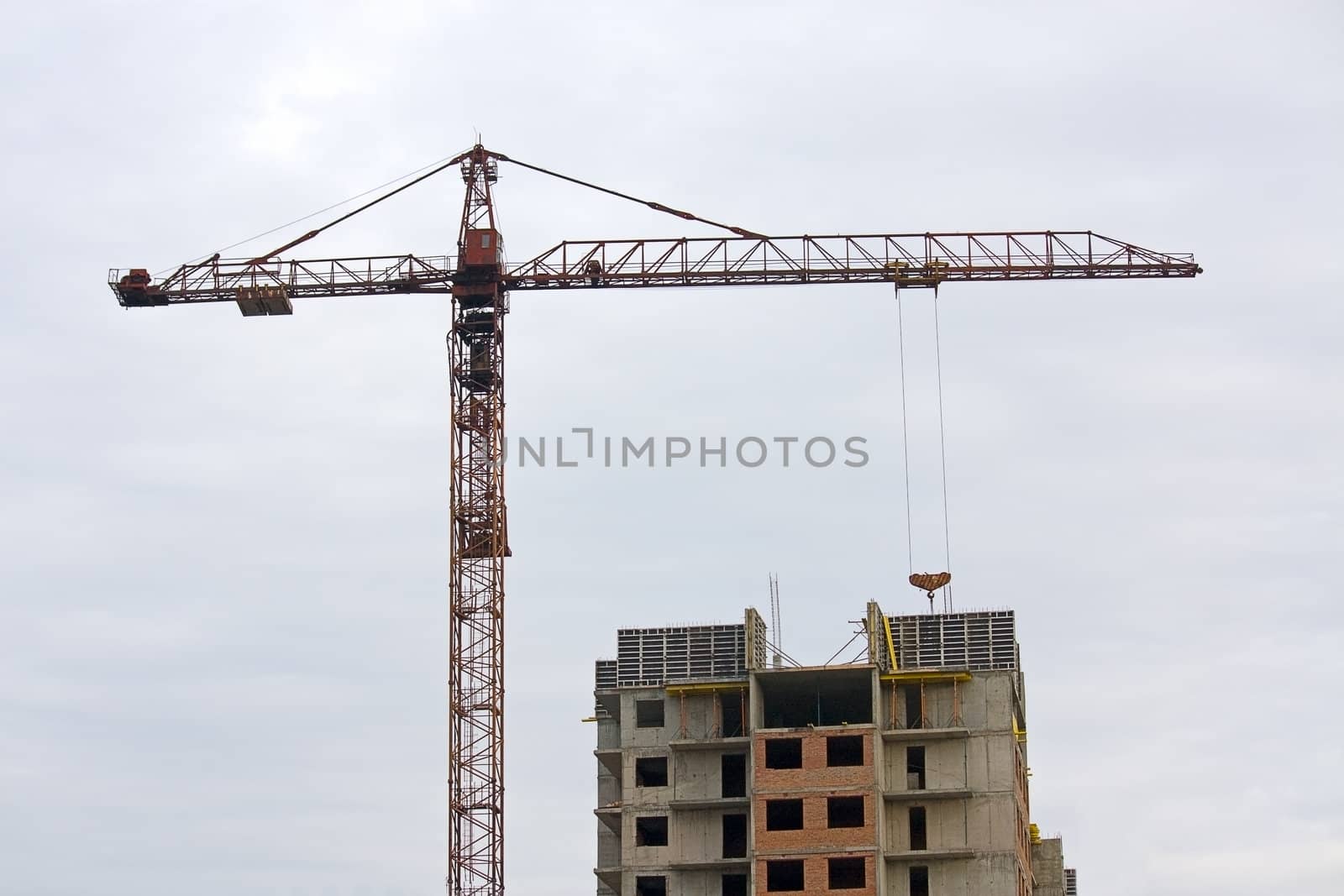 Tower crane near the house under construction on the background of a cloudy sky