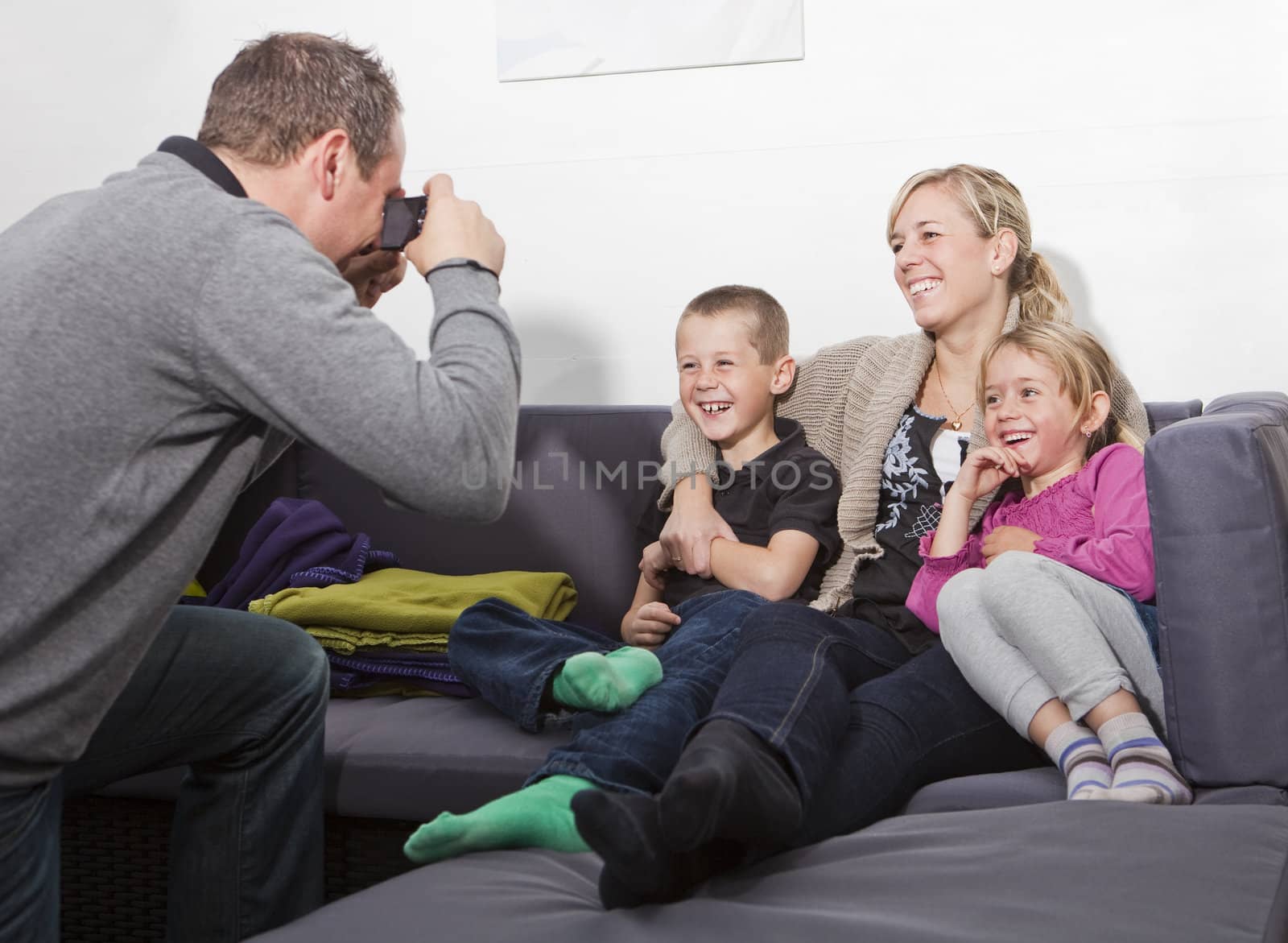 Father taking a photo of his family siting in the sofa