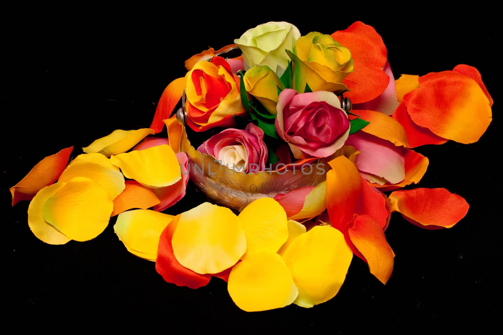 A silver basket with artificial roses on orange, yellow and pink rose textile petals on black
