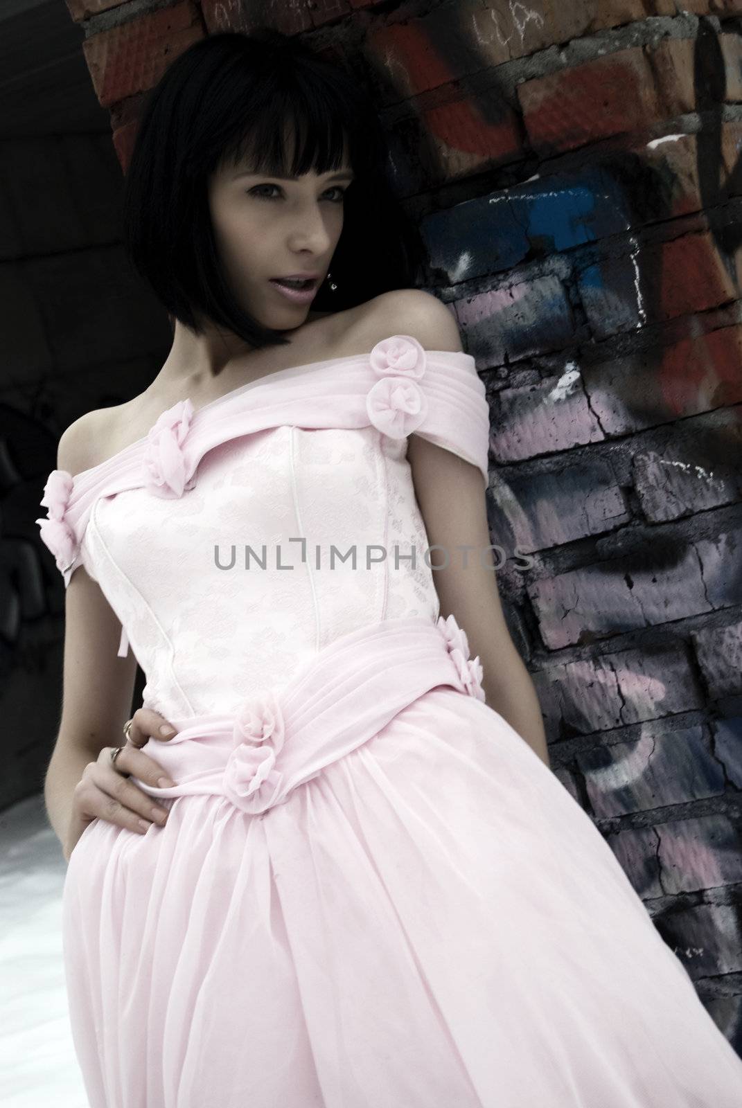 young bride in pink wedding dress standing among street ruins