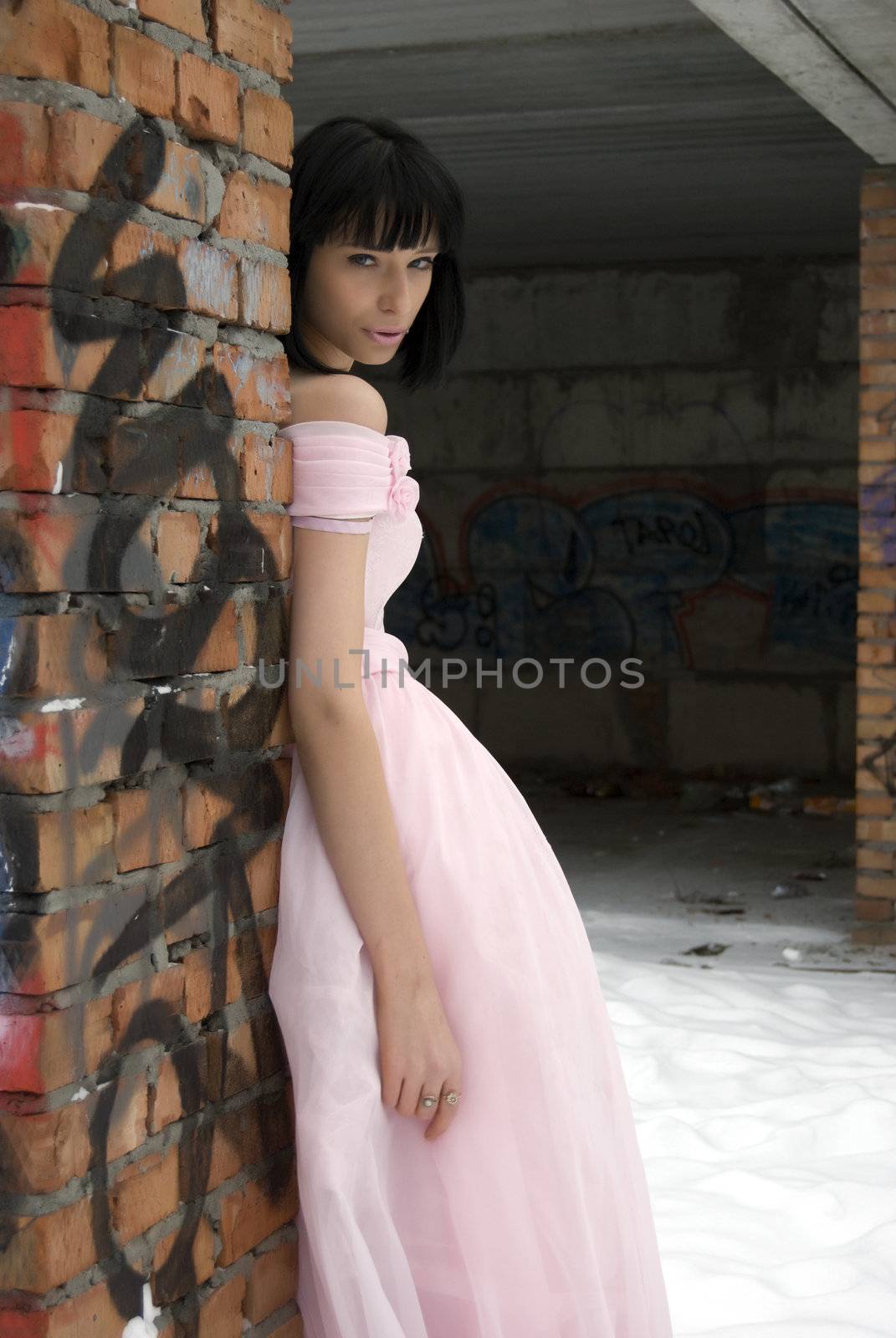 young bride in pink wedding dress standing among street ruins