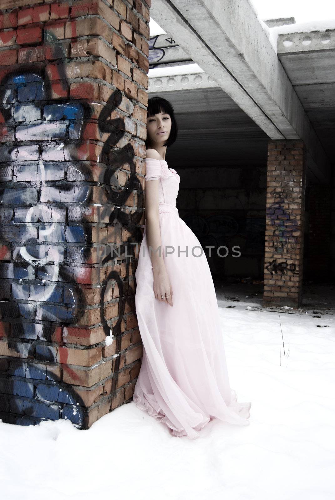young bride in pink wedding dress standing among street ruins