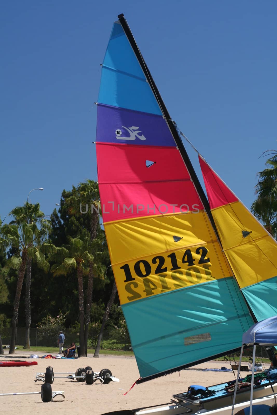 A color sail boat on a white sand beach.