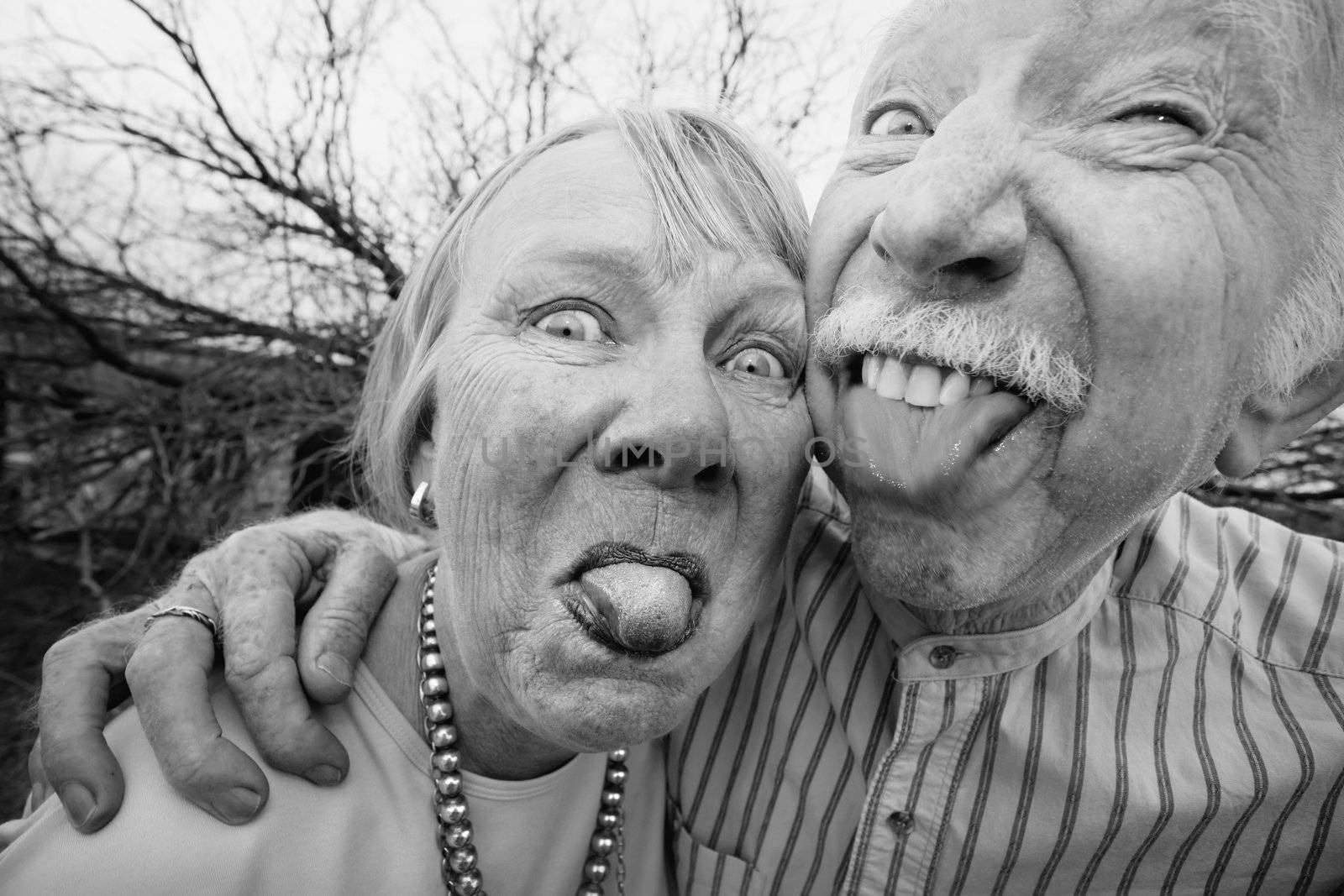 Closeup portrait of crazy elderly couple outdoors sticking out tongues