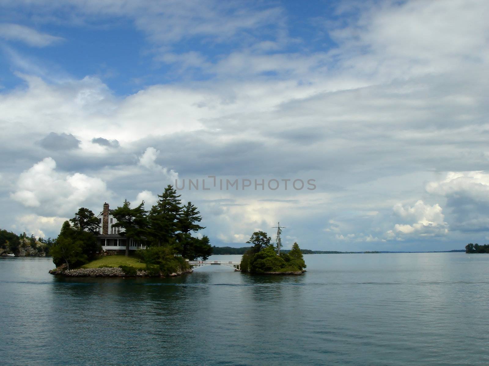 Two islands with a little bridge between and a cross on it and a house on the other between the thousand islands on the Ontario lake, Canada, by cloudy weather