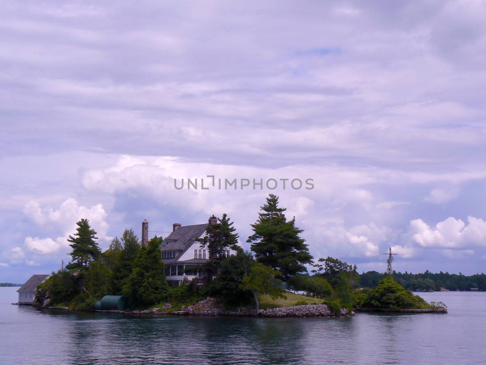 Two islands with a little bridge between and a cross on it and a house on the other between the thousand islands on the Ontario lake, Canada, by cloudy weather