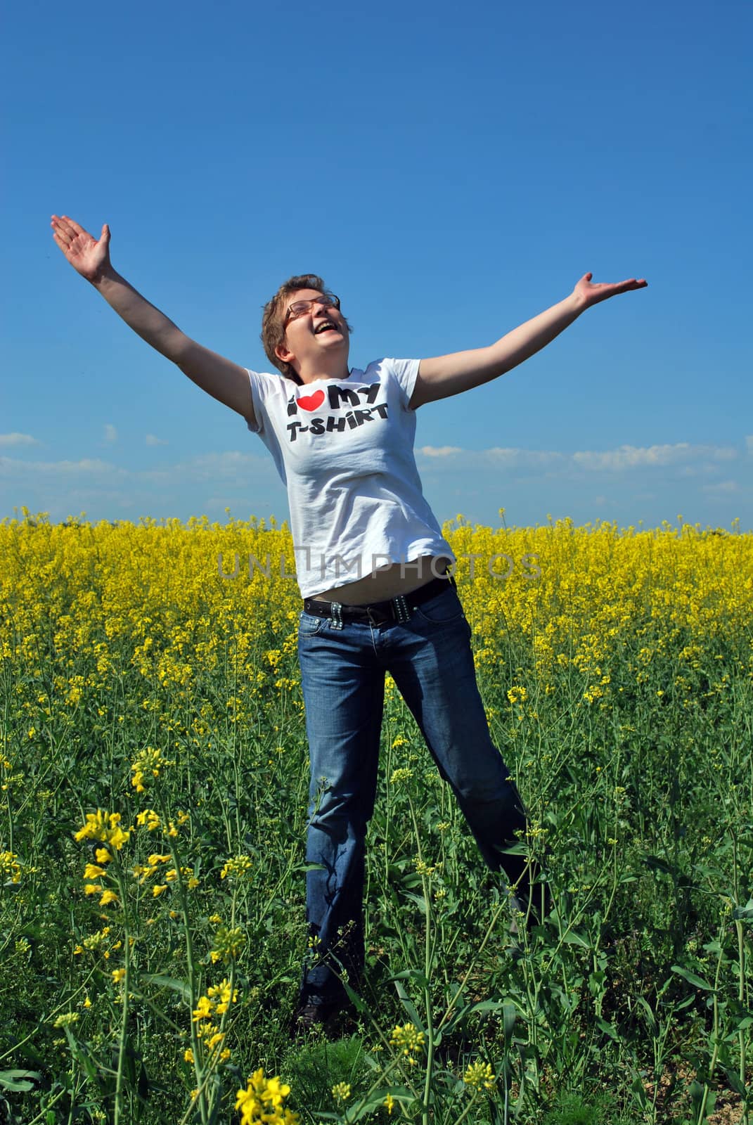 young woman jumping in nature with yellow field and blue sky