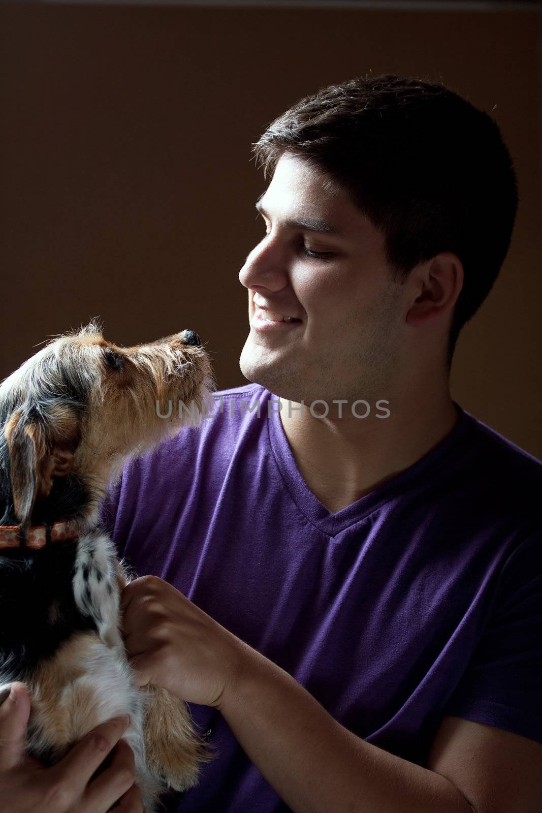 Low key portrait of a young man holding a cute mixed breed terrier dog isolated over a dark background.